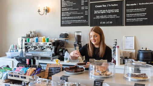 Aelod o staff yn gweithio tu ôl i'r cownter yn y caffi yn Dinefwr, Sir Gaerfyrddin